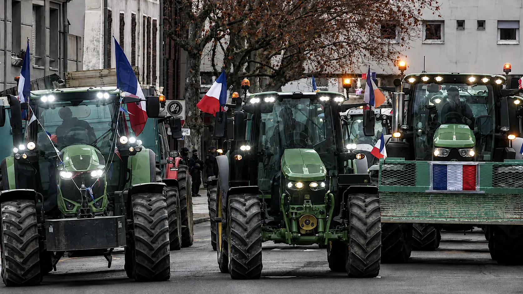 Convoi de tracteurs aux drapeaux français dans une rue, mobilisation d’agriculteurs