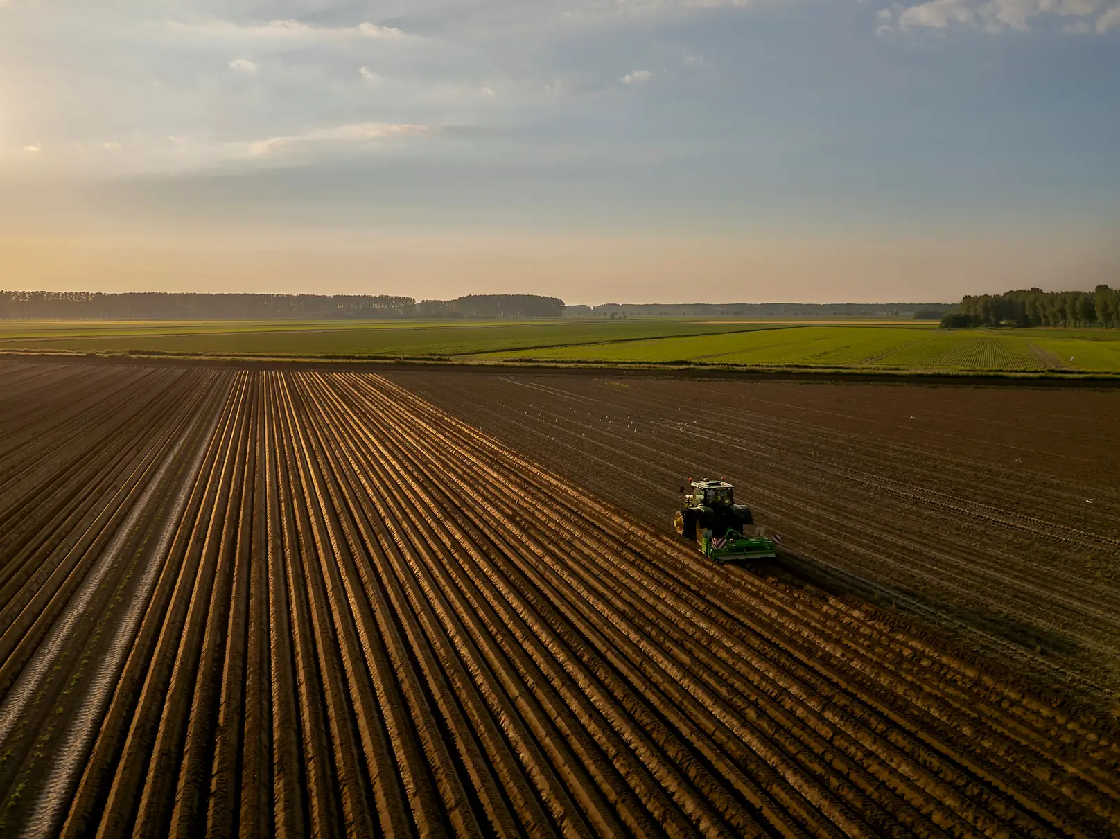 Vue aérienne d’un tracteur au travail sur une grande parcelle labourée, au lever du soleil