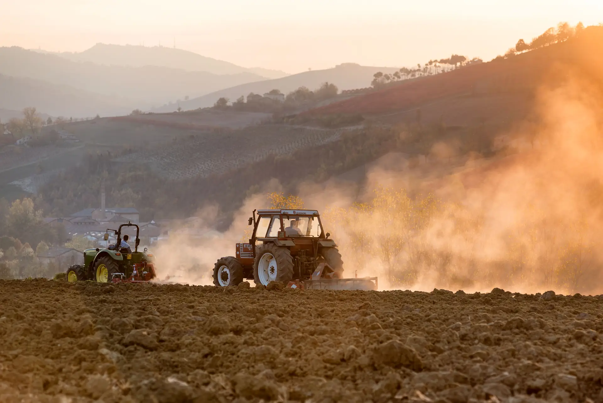 Tracteurs au travail sur un coteau, dans un nuage de poussière à la lumière du soir