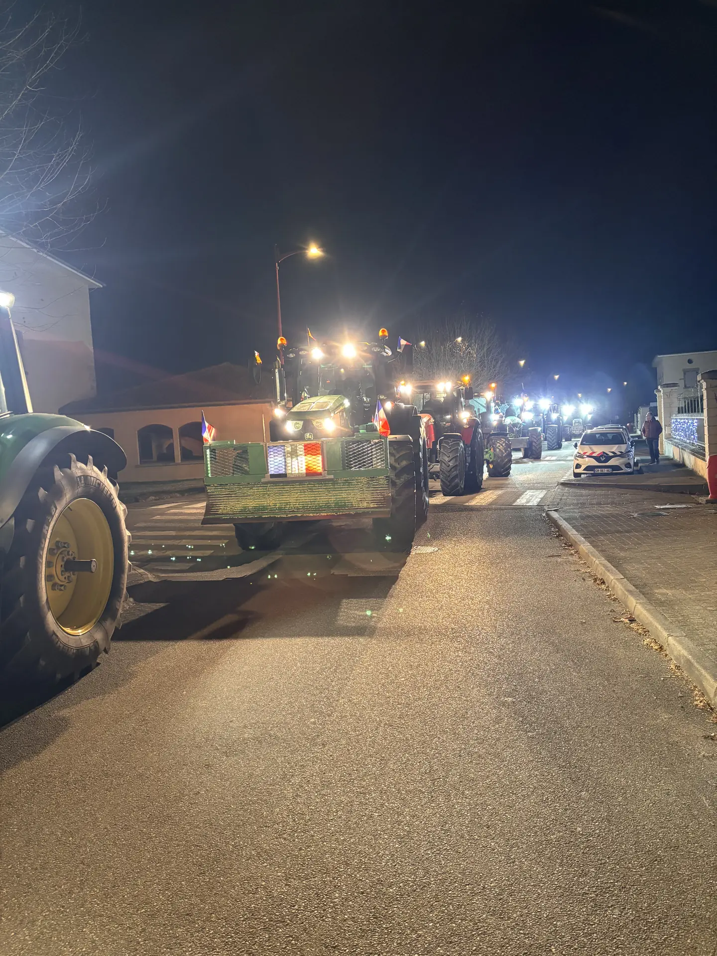 Rue éclairée de nuit où stationnent des tracteurs, mobilisation à Reventin-Vaugris